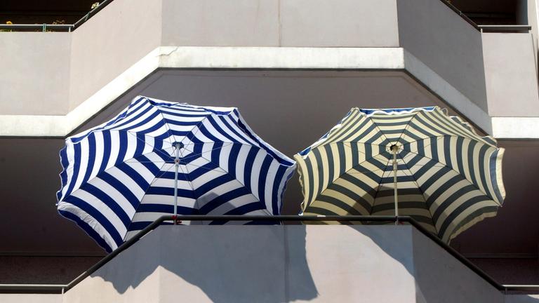 Zwei Sonnenschirme ragen aus der Beton-Fassade eines Hochhauses.