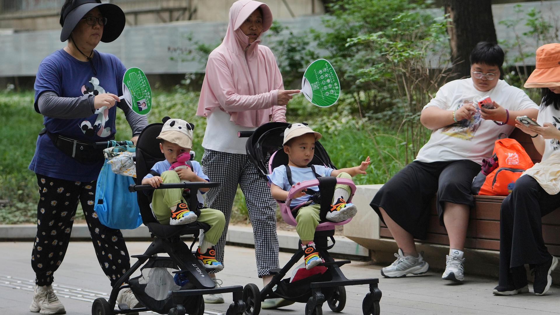 Frauen fächeln ihren Kindern im Kinderwagen Luft zu, während sie an einem schwülen Tag in Peking am Dienstag, dem 22. Juli 2025, eine Straße entlanggehen. 