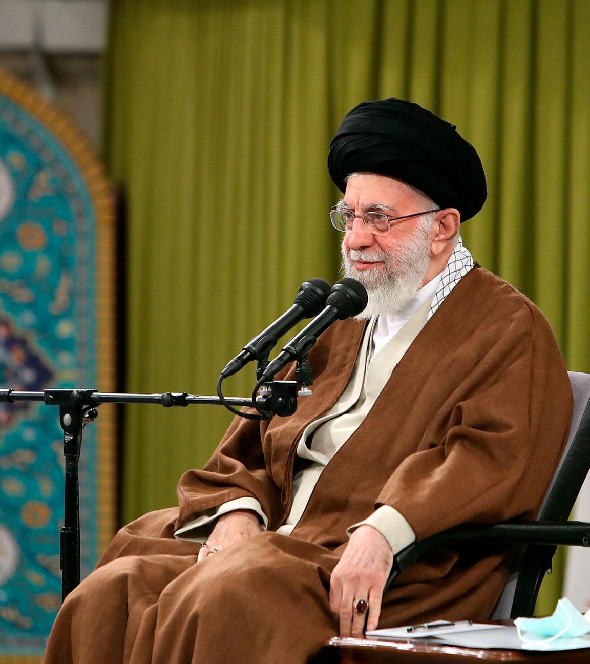 Ajatollah Ali Chamenei sitzt vor einem Mikrofon, im Hintergrund die iranische Flagge. 