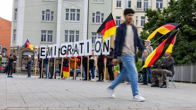 Ein Mann geht an Demonstranten vorbei, die Buchstaben des Schriftzugs "Remigration" hochhalten.