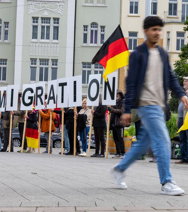 Ein Mann geht an Demonstranten vorbei, die Buchstaben des Schriftzugs "Remigration" hochhalten.