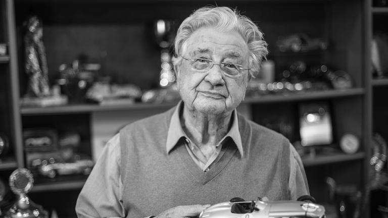 Graues Bild von Hans Herrmann mit einem Modellauto in der Hand