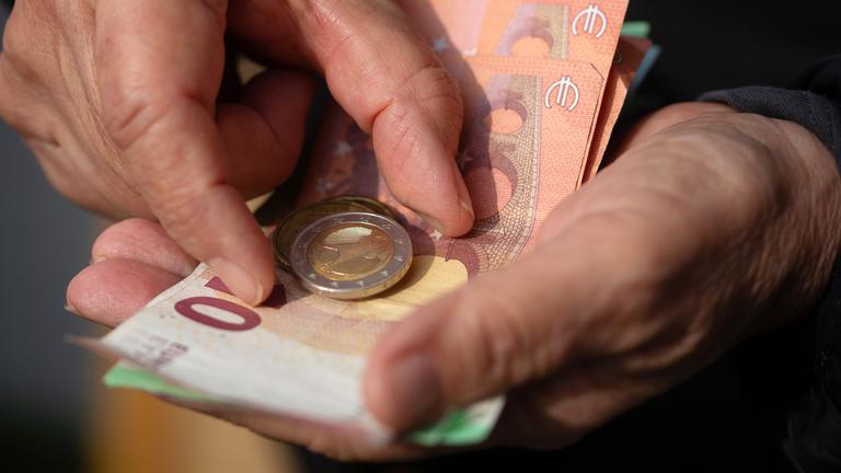 Eine Seniorin hält Euro-Banknoten und Münzen in der Hand
