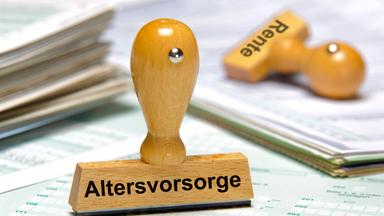 Ein Holzstempel ist beschriftet mit dem Aufdruck Altersvorsorge. Im Hintergrund liegt ein weiterer Stempel mit dem Aufdruck Rente.