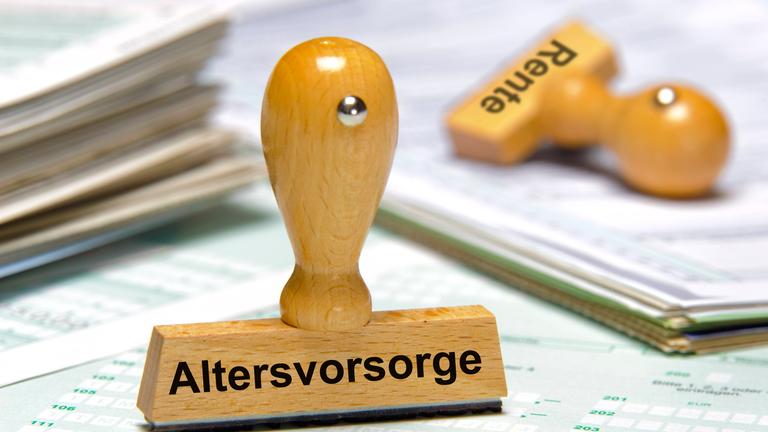 Ein Holzstempel ist beschriftet mit dem Aufdruck Altersvorsorge. Im Hintergrund liegt ein weiterer Stempel mit dem Aufdruck Rente.