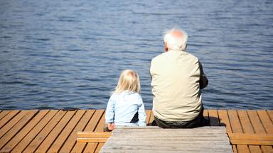Großvater und Enkelin sitzen am Ufer eines Sees