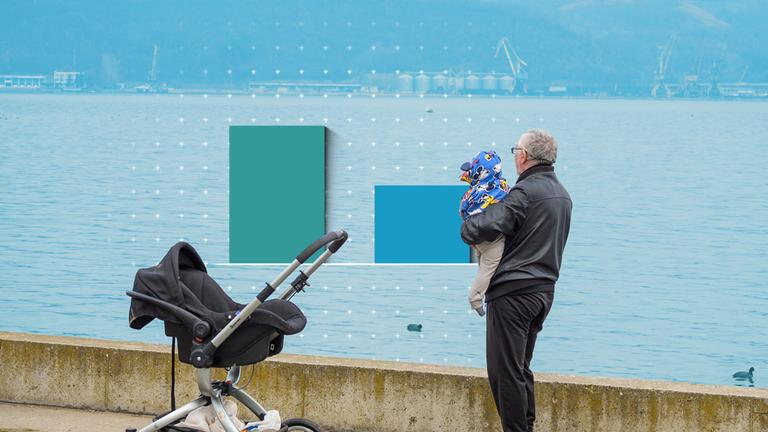 Ein Mann hält ein Baby, im Hintergrund ist Wasser zu sehen.