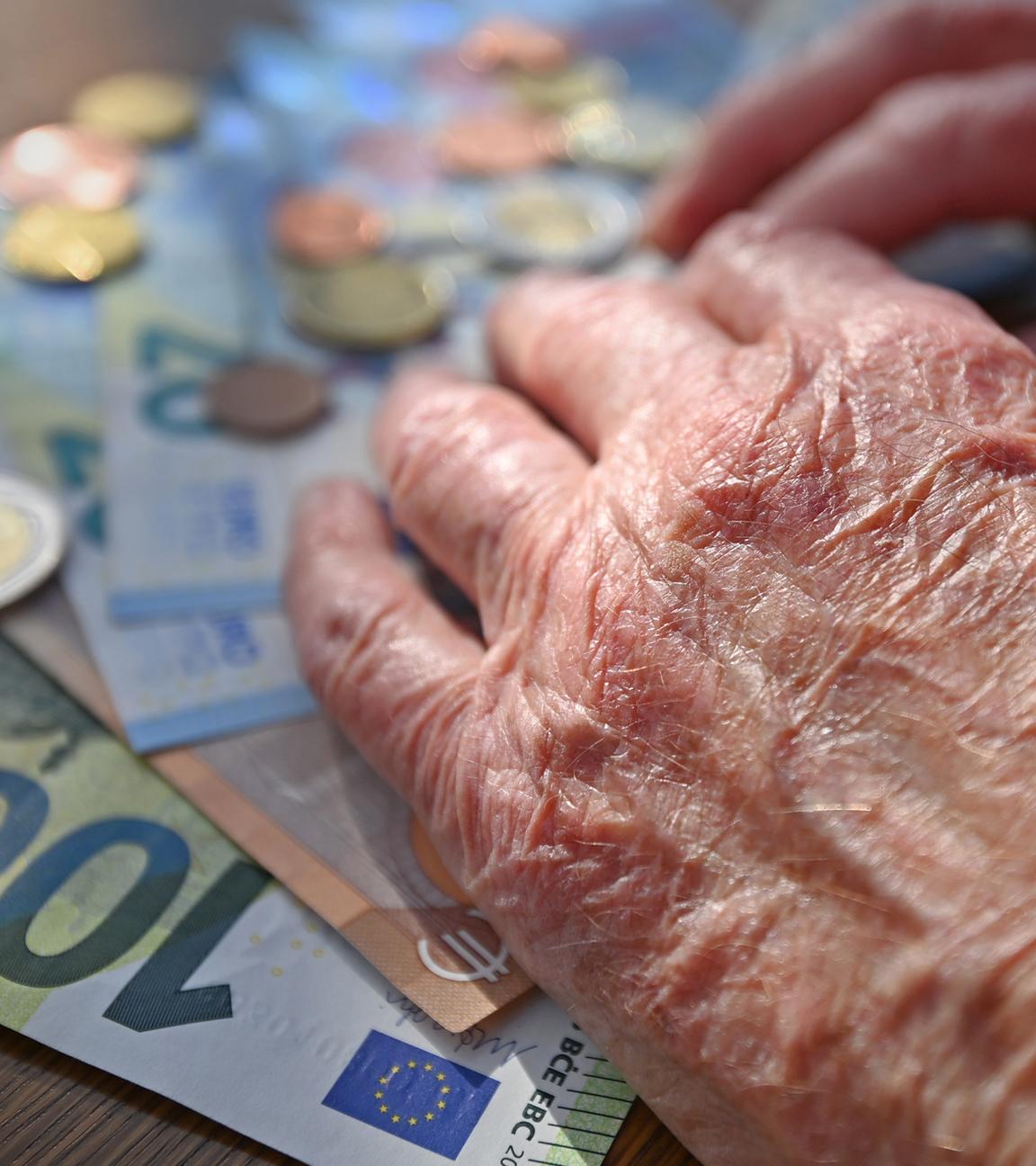 Hand einer alten Frau, die auf einem Tisch mit Scheinen und Münzen Geld zählt