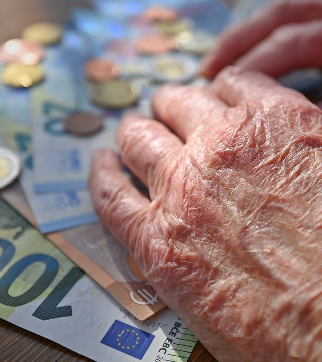 Hand einer alten Frau, die auf einem Tisch mit Scheinen und Münzen Geld zählt