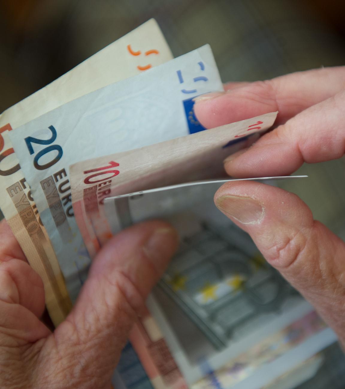 Es sind Hände einer älteren Person zu sehen, die Geldscheine hält.