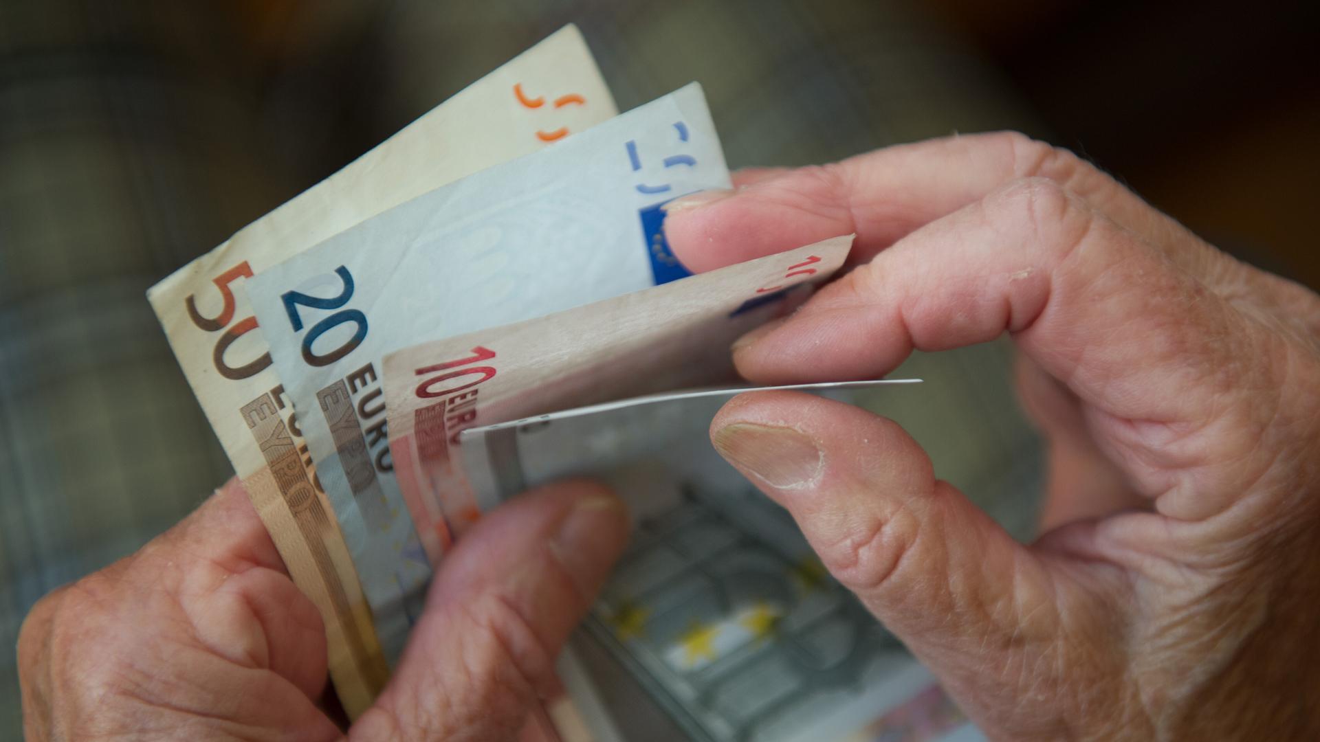 Es sind Hände einer älteren Person zu sehen, die Geldscheine hält.