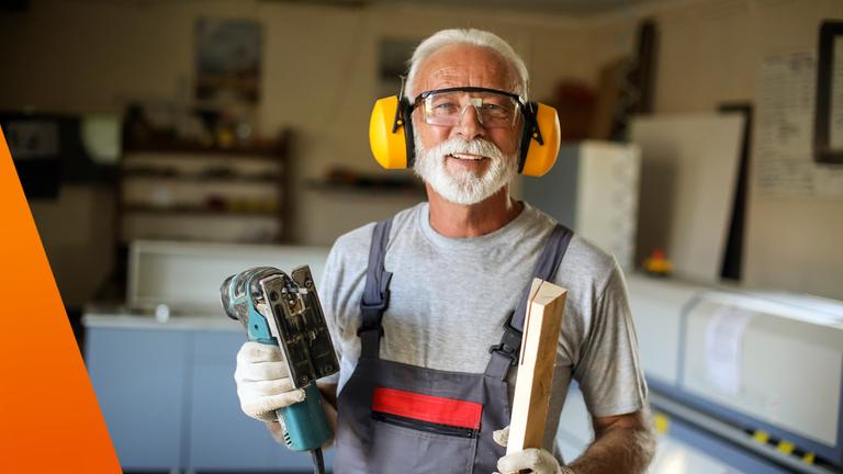 Älterer Mann mit Säge und Brett in der Hand