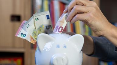 Eine Frau steckt einen 10-Euro-Schein in ein Sparschwein.