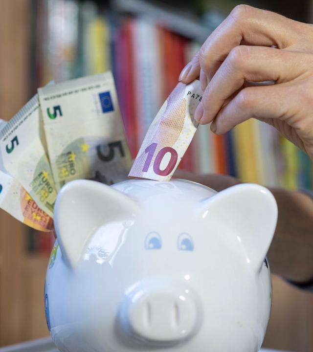 Eine Frau steckt einen 10-Euro-Schein in ein Sparschwein.