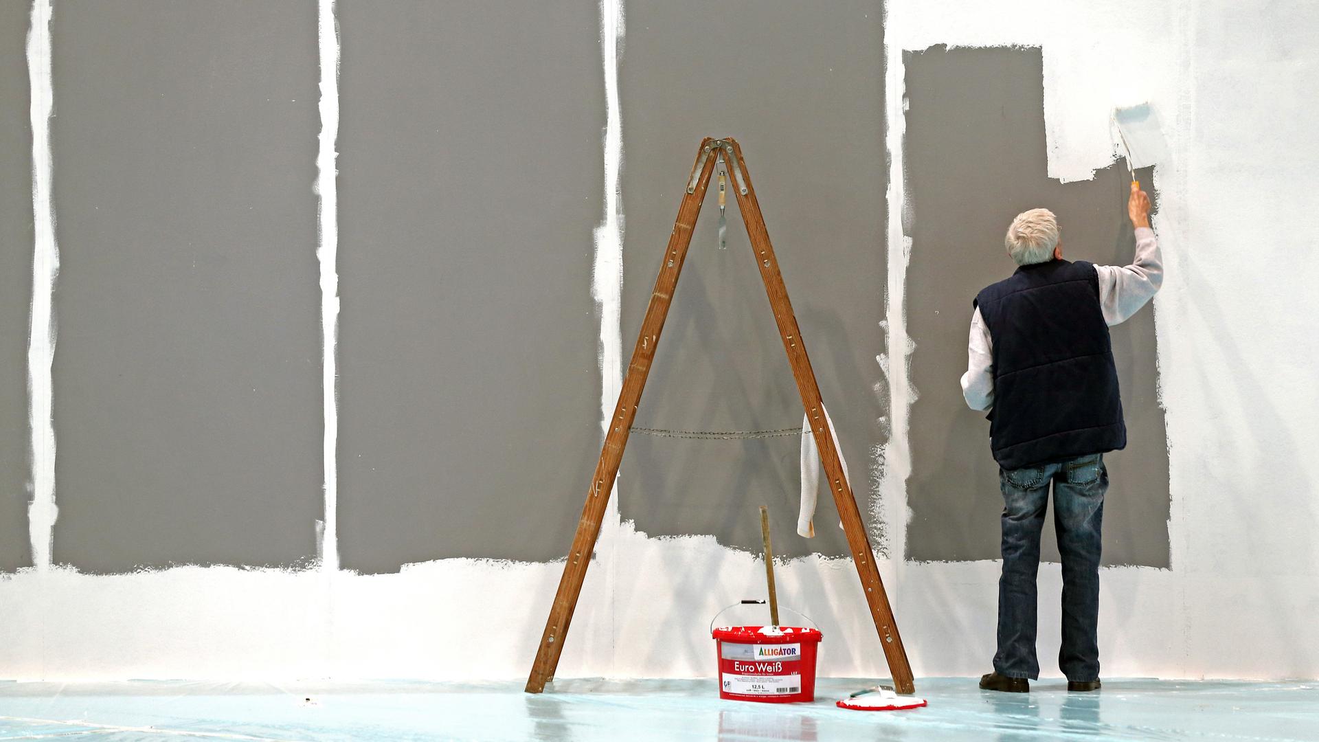 Ein älterer Herr mit grauen Haaren streicht auf der Leipziger Messe eine Wand. Archivbild