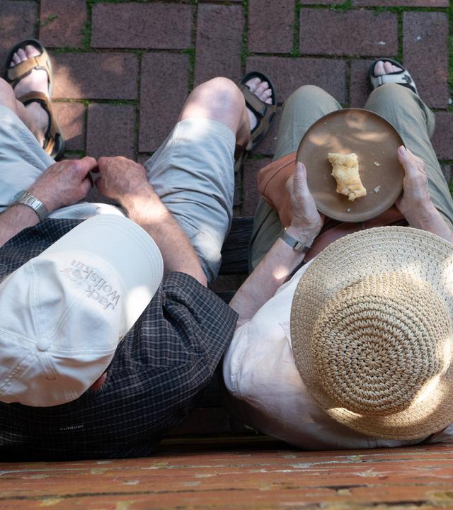Zwei Senioren sitzen auf einer Bank und essen Kuchen.