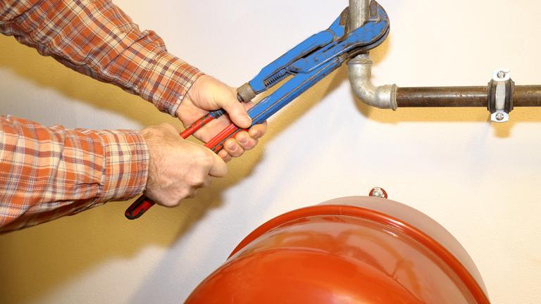 Mann hält Zange an ein Heizungsrohr