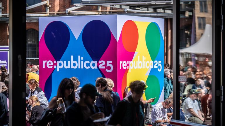 Besucher der Medienkonferenz Re:publica sitzen an einem Logo-Aufsteller am Veranstaltungsort «Station Berlin».