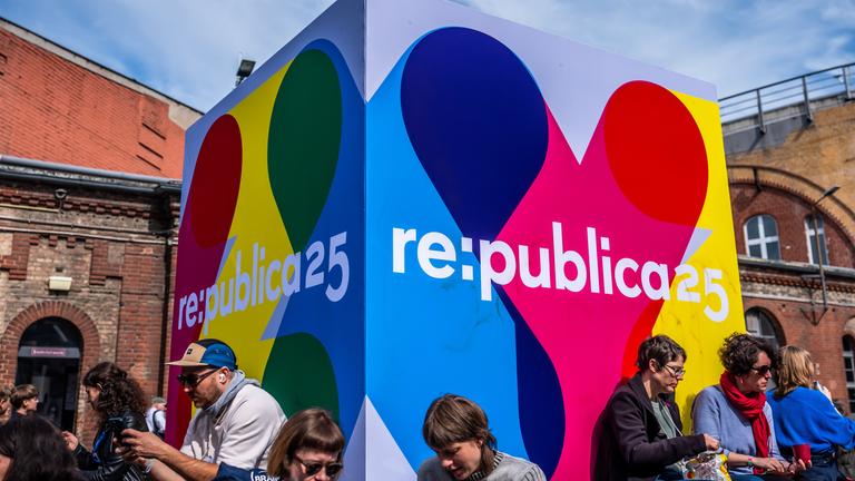  Besucher der Medienkonferenz Re:publica sitzen an einem Logo-Aufsteller vor der Eröffnung vor dem Veranstaltungsort 
