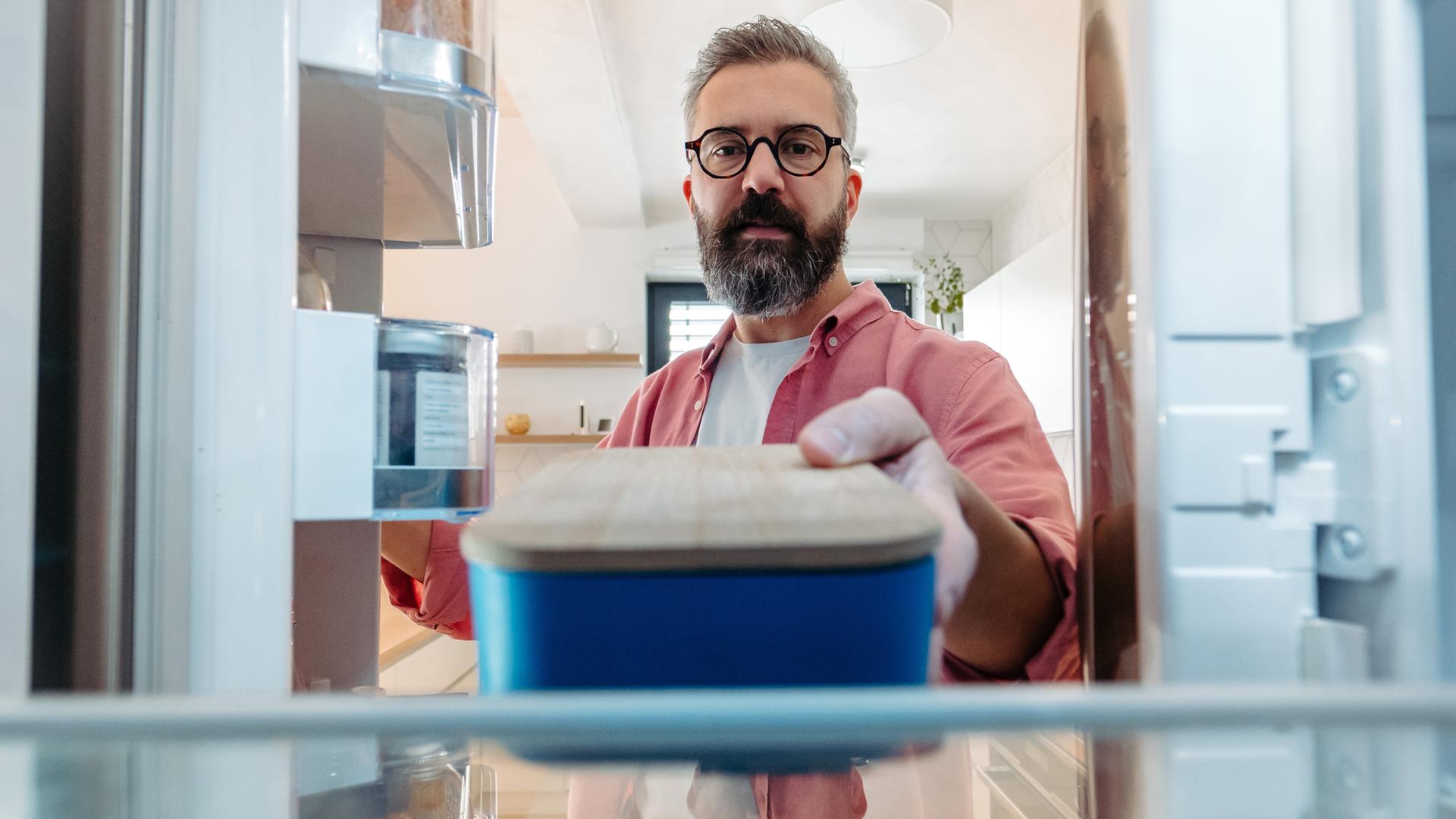 Mann stellt Lunchbox in den Kühlschrank.