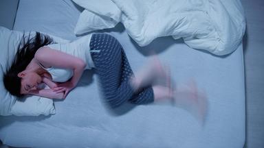 Eine Frau mit RLS , dem Restless Legs Syndrom, schläft in ihrem Bett.