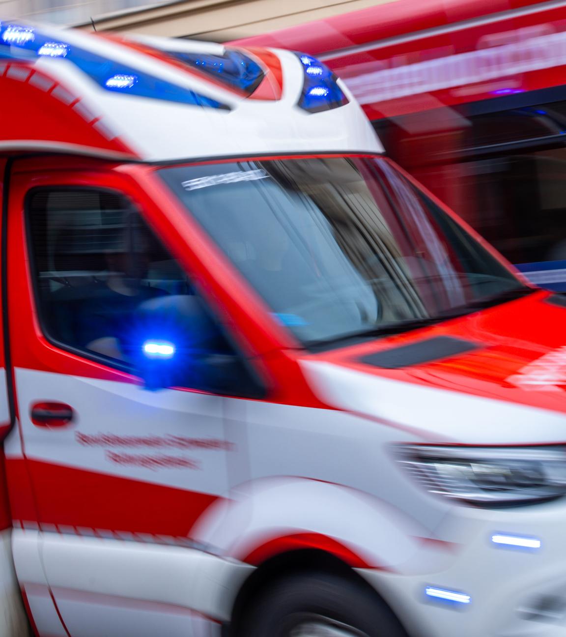 Ein Rettungsfahrzeug ist mit Blaulicht auf einer Straße in der Innenstadt unterwegs.