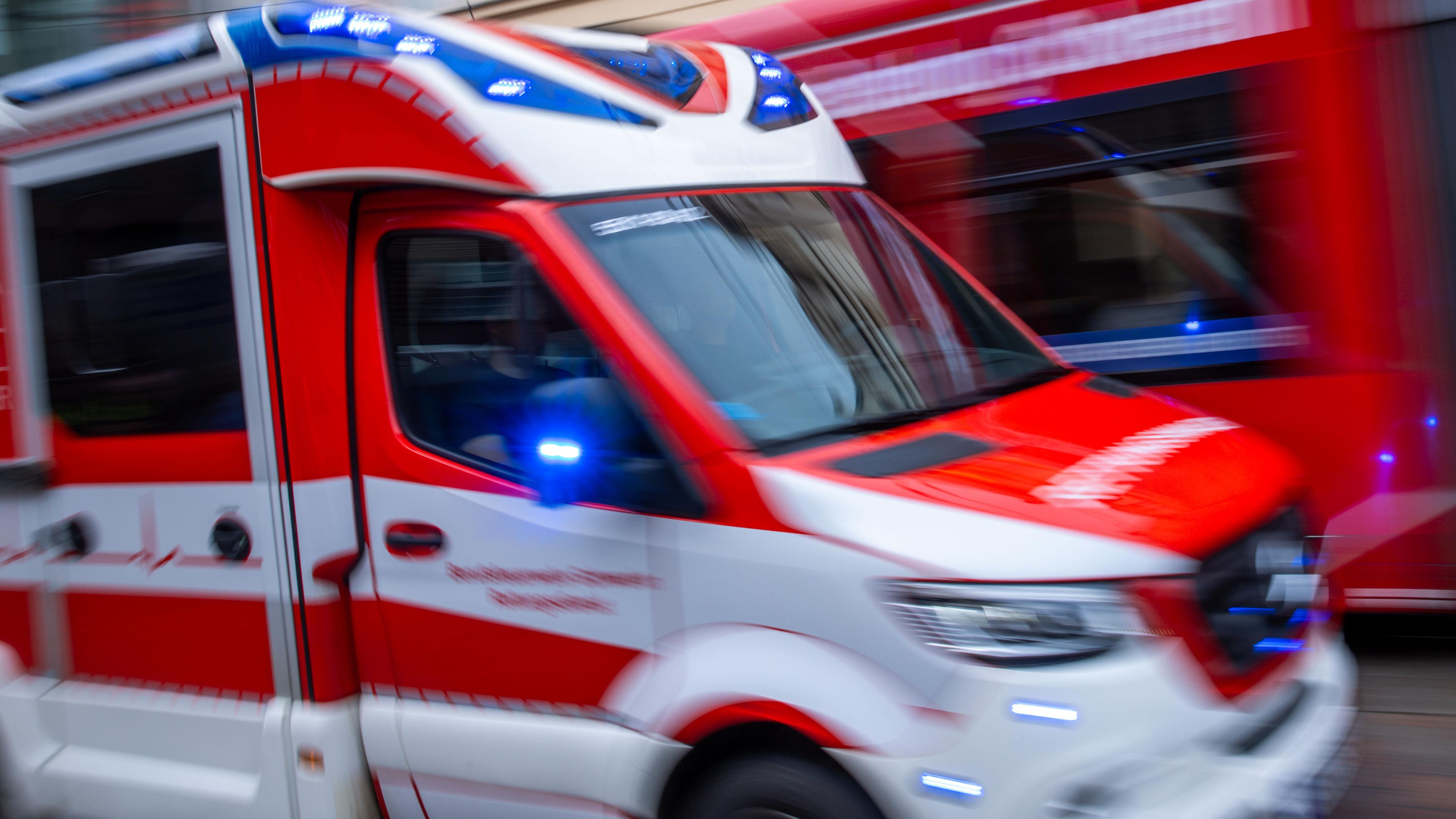 Ein Rettungsfahrzeug ist mit Blaulicht auf einer Straße in der Innenstadt unterwegs.