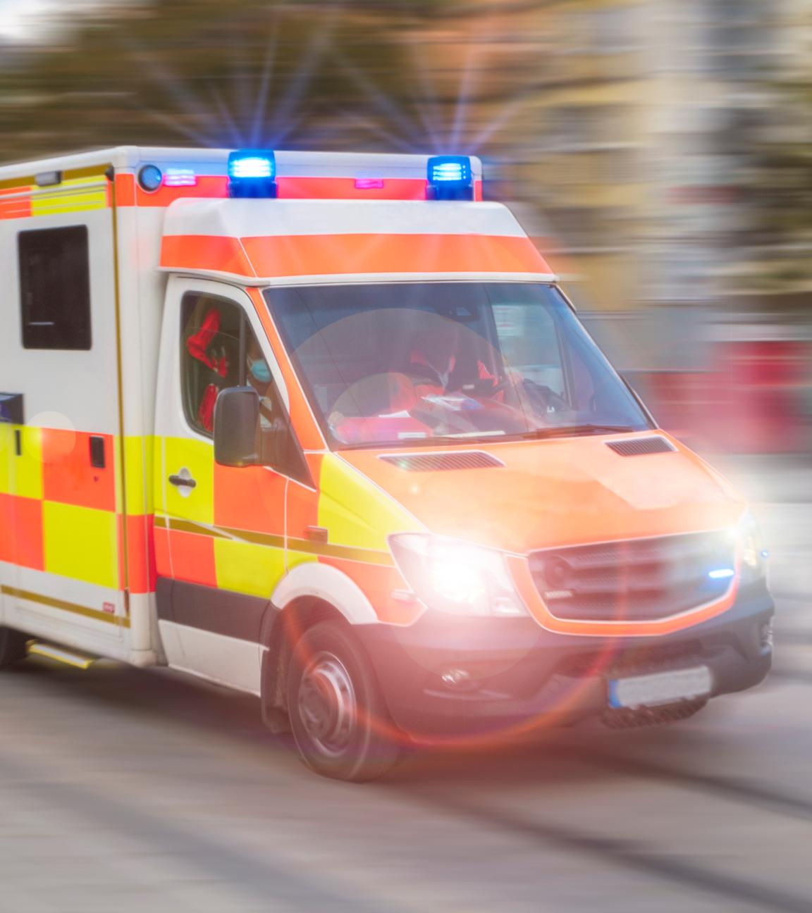 Ein Rettungsfahrzeug vom Roten Kreuz fährt mit Blaulicht und hoher Geschwindigkeit durch die Stadt.