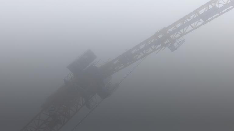 Ein Kran steht bei dichtem Nebel in einem Rohbau für Eigentumswohnungen im Stadtteil Ehrenfeld. 