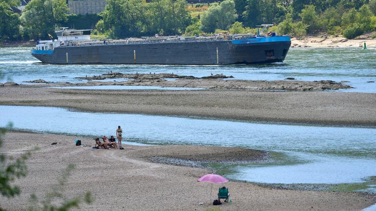 Rheinland-Pfalz, St. Goarshausen: Touristen entspannen sich auf einer Sandbank im Rhein nahe der Loreley, während ein Frachtschiff vorbeifährt.