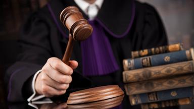 Eine Person in Richterrobe hält einen Holzhammer in der Hand, im Hintergrund liegen Bücher.