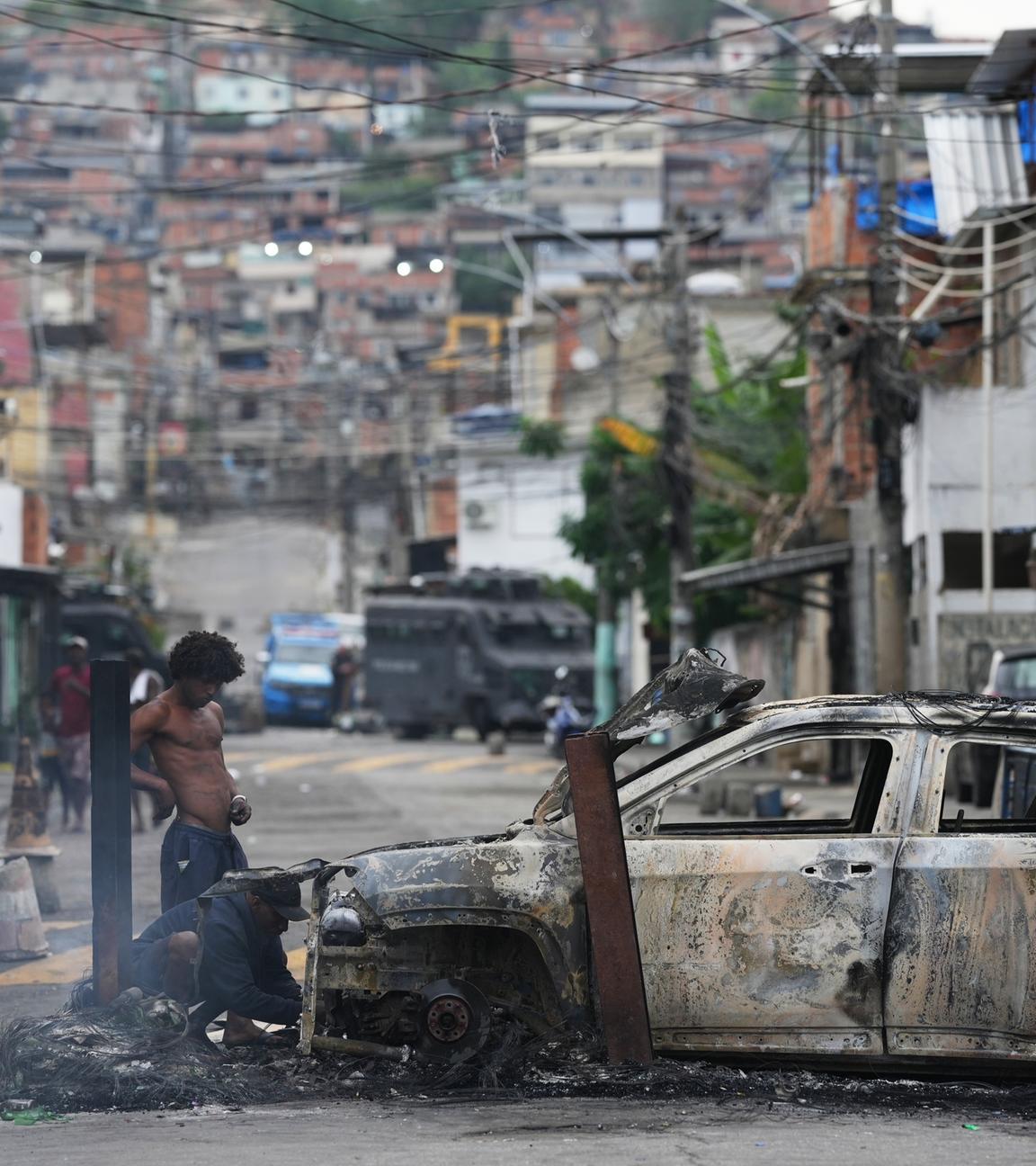 Menschen entfernen nützliche Teile aus einem verbrannten Auto während eines Polizeieinsatzes. Bei einem Großeinsatz der Polizei in der Favelas Alemao und dem Viertel Penha im Norden von Rio seien mehrere mutmaßliche Gangmitglieder festgenommen worden.
