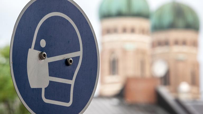ein schild fordert am viktualienmarkt in der münchner innenstadt zum tragen einer mund und nasen bedeckung auf