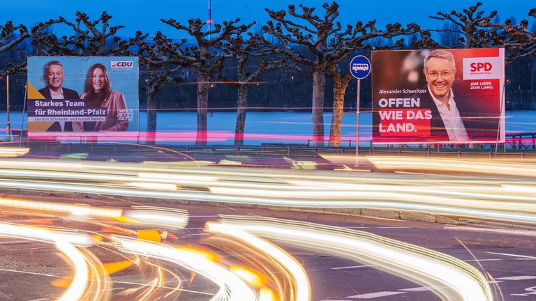  Vorbeifahrende Fahrzeuge erzeugen auf der Rheinallee Lichtstreifen vor den Wahlplakaten von Gordon Schnieder, CDU-Landeschef und Spitzenkandidat seiner Partei zur anstehenden Landtagswahl, mit Isabell Rahms, Landtagskandidatin ihrer Partei für Mainz zur anstehenden Landtagswahl, und Alexander Schweitzer.
