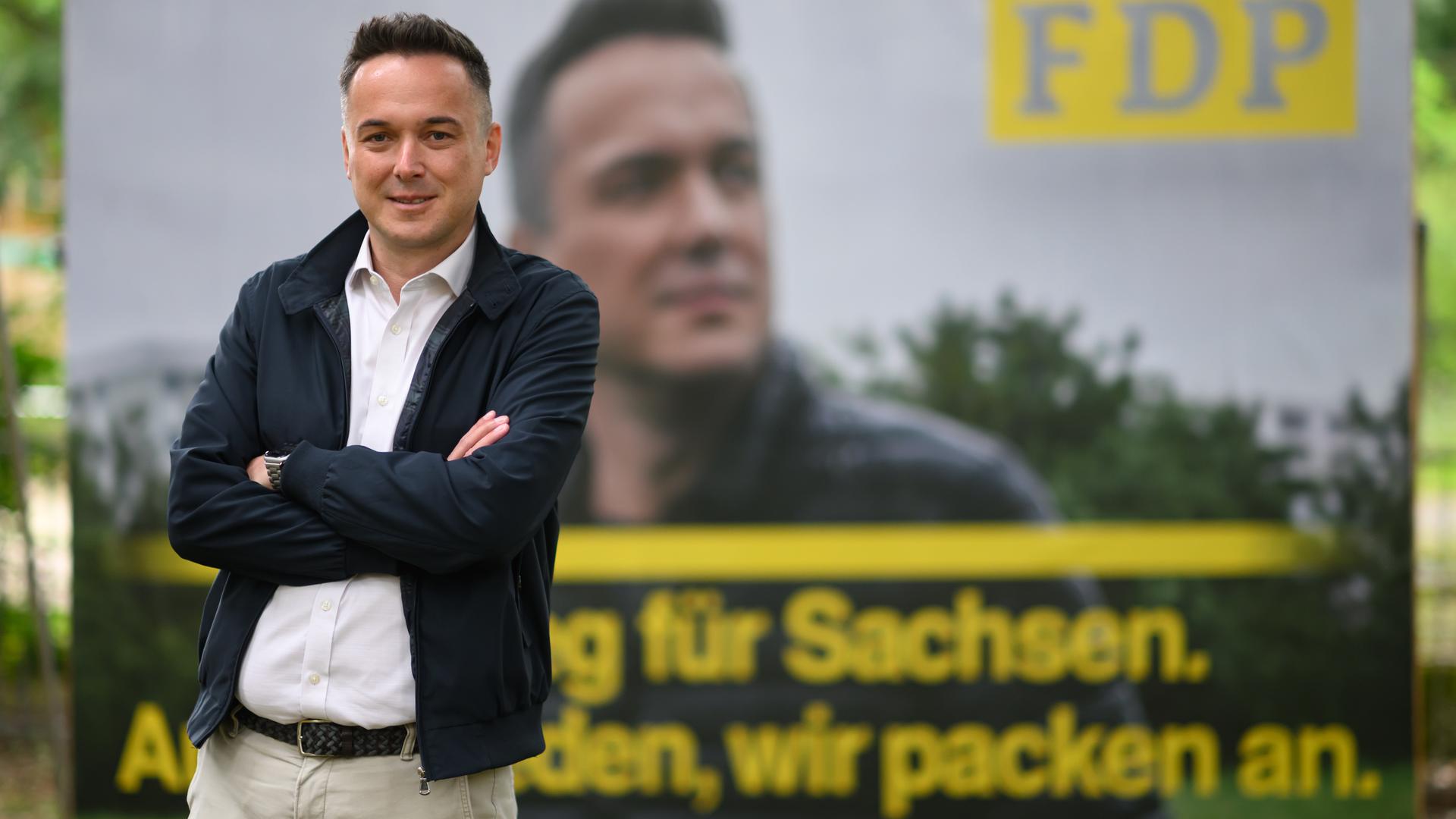 Robert Malorny steht mit verschränkten Armen vor seinem eigenen Wahlkampfplakat. 