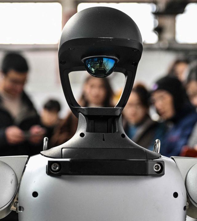 Ein humanoider Roboter wird bei einer Messe von Menschen umringt, die ihn betrachten.