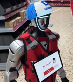 Roboter "Schotti" mit blauer Kappe und roter Weste steht im Baumarkt.