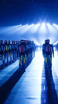 110 humanoide Roboter stehen in Reihen aufgestellt und leuchten.