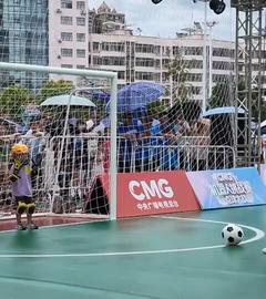 Ein Kind steht im einem kleinen Fußballtor (links), ein kleiner Roboter steht einige Meter vor dem Tor (rechts), vor ihm liegt ein Fußball.