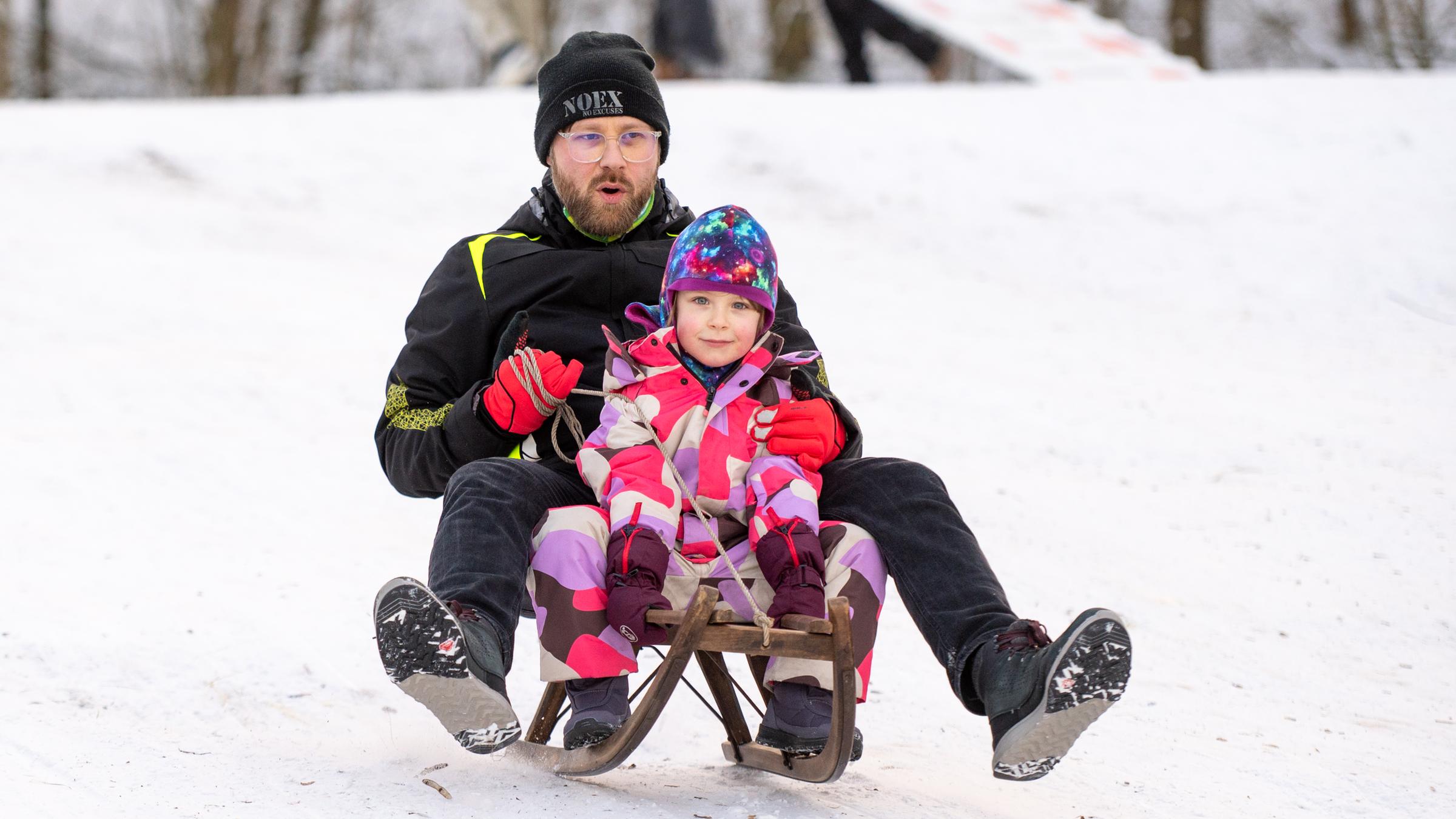 Ein Vater sitzt mit seinem Kind auf einem Schlitten und rodelt am Teufelsberg in Berlin.