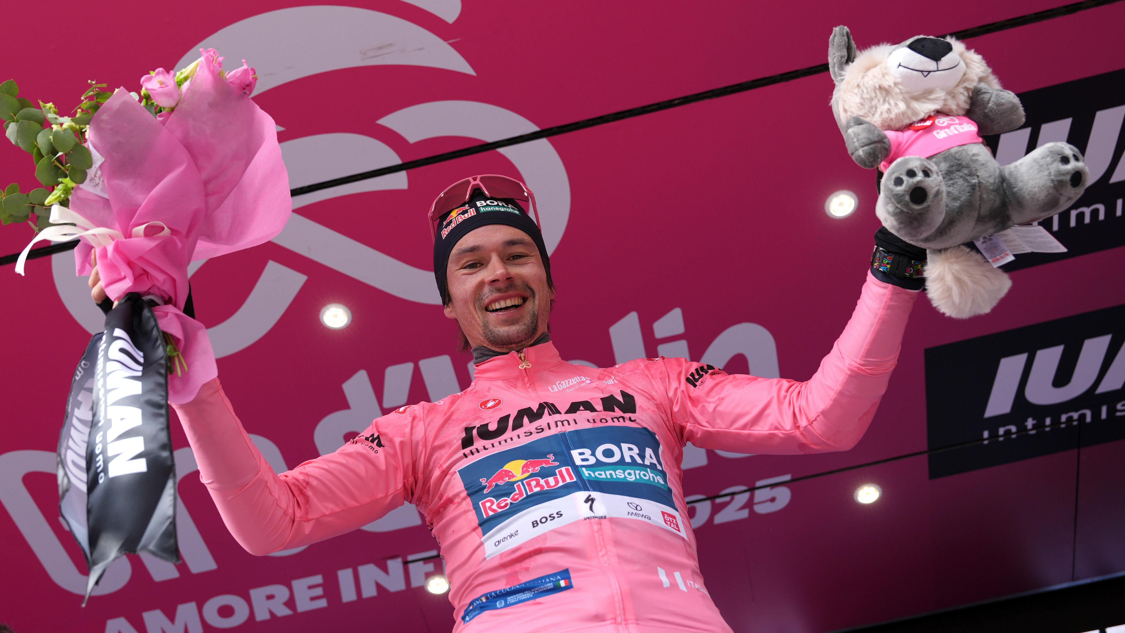 Primoz Roglic hält bei der Siegehrung einen Blumenstrauß und ein Maskottchen in die Höhe
