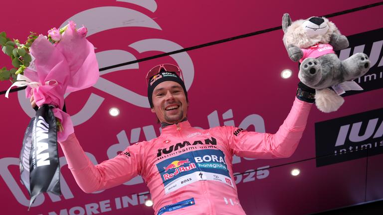 Primoz Roglic hält bei der Siegehrung einen Blumenstrauß und ein Maskottchen in die Höhe