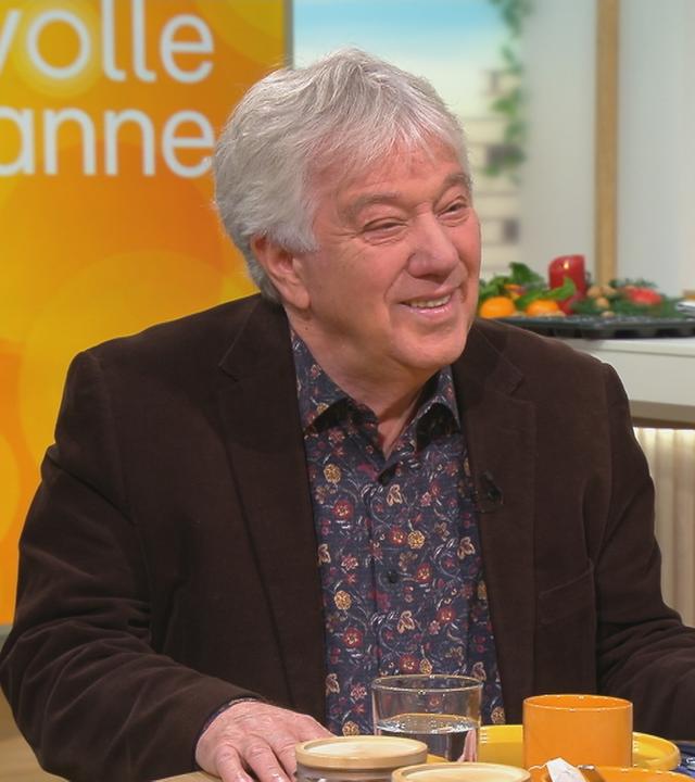 Musiker Rolf Zuckowski sitzt bei Volle Kanne im Studio am Frühstückstisch.