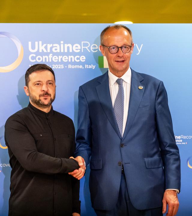 Bundeskanzler Friedrich Merz (CDU, r) und Wolodymyr Selenskyj, Präsident der Ukraine, geben sich vor einem bilateralen Gespräch bei der Wiederaufbaukonferenz für die Ukraine die Hand.