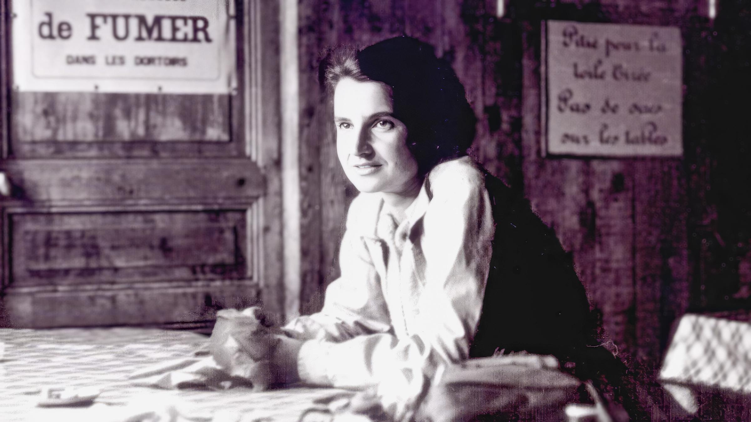 Schwarz-Weiß-Foto von Rosalind Franklin, die sich mit den Armen auf einem Tisch abstützt.