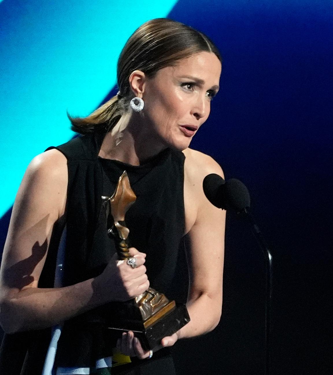 Rose Byrne mit Trophäe in der Hand, während sie anlässlich ihrer Laudatio ins Mikrofon spricht.