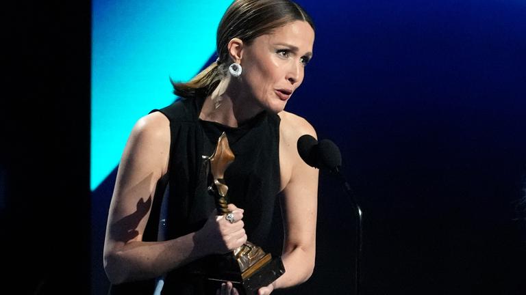 Rose Byrne mit Trophäe in der Hand, während sie anlässlich ihrer Laudatio ins Mikrofon spricht.
