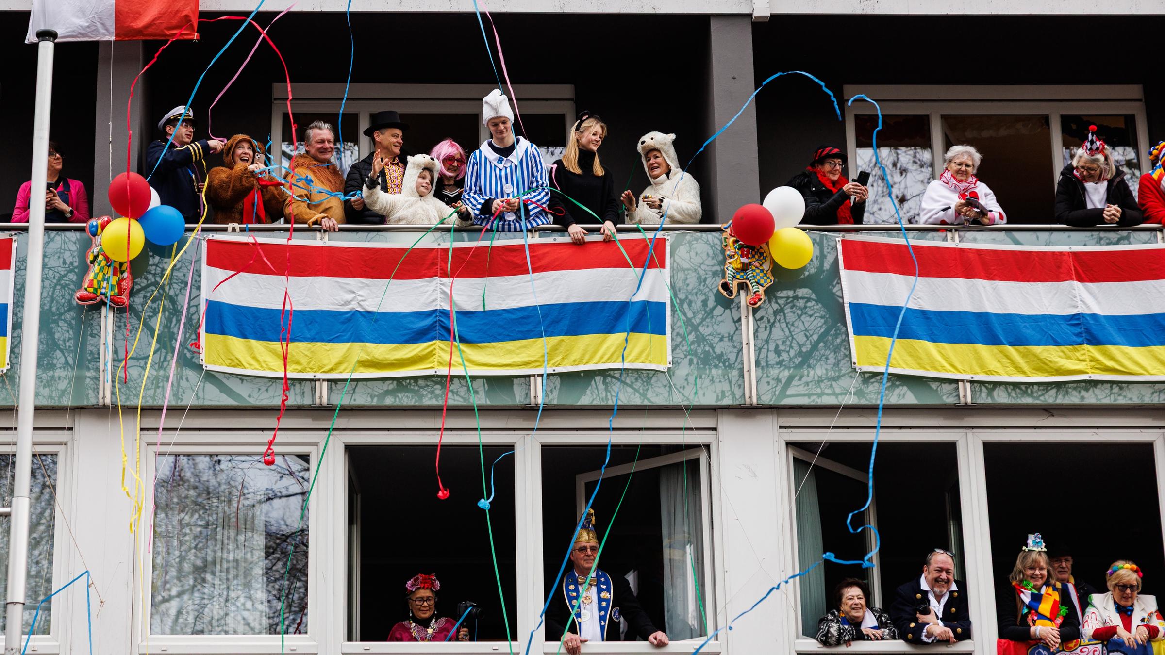 Verkleidetete Menschen verfolgen von ihren Fenstern den Mainzer Rosenmontagszug.