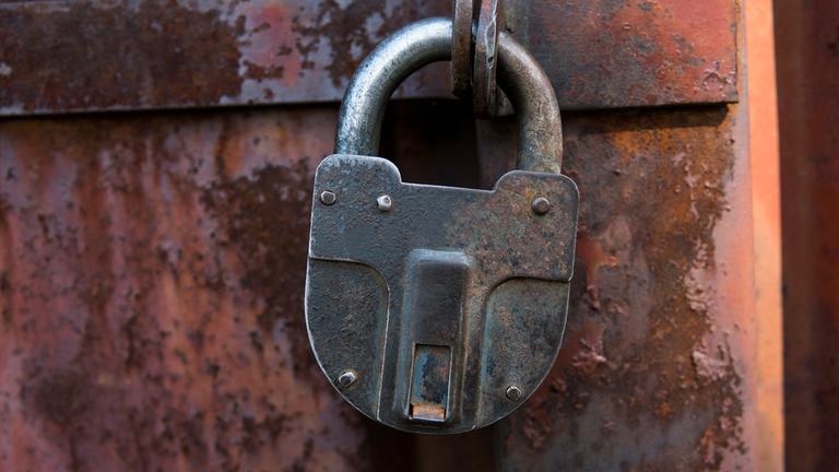 Vorhängeschloss hängt an einer rostigen Tür