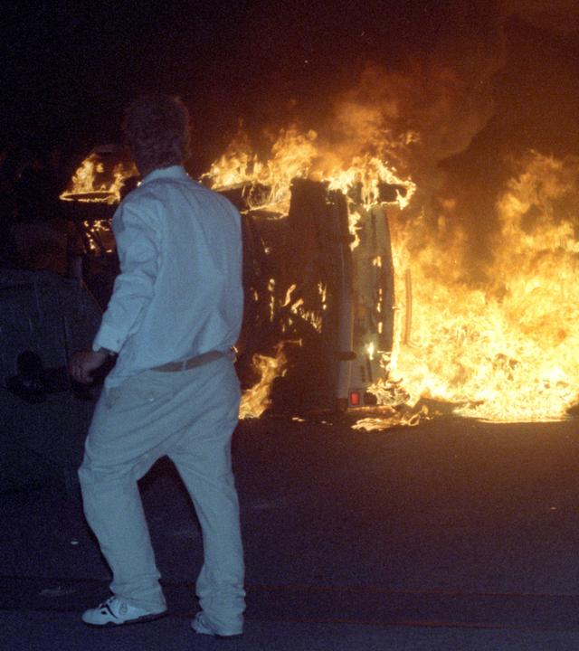 Ein Randalierer steht vor einem brennenden Trabi in Rostock-Lichtenhagen